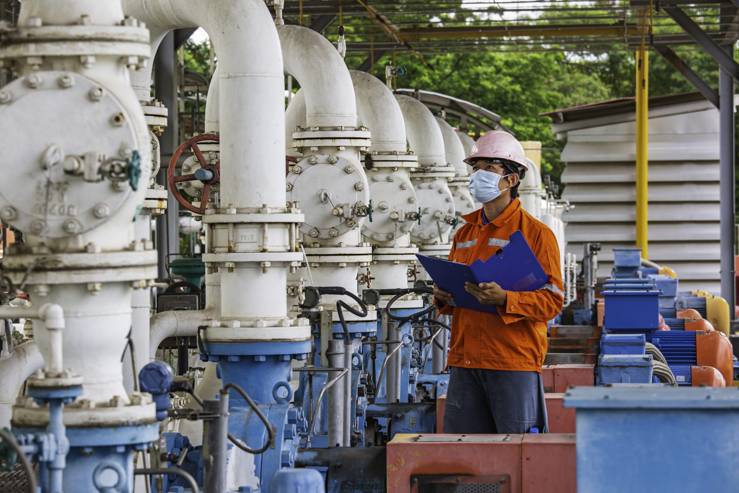 Male worker inspection pump motor oil at steel long pipes and pipe elbow in station oil factory during refinery valve of visual check record pipeline tank oil and gas industry